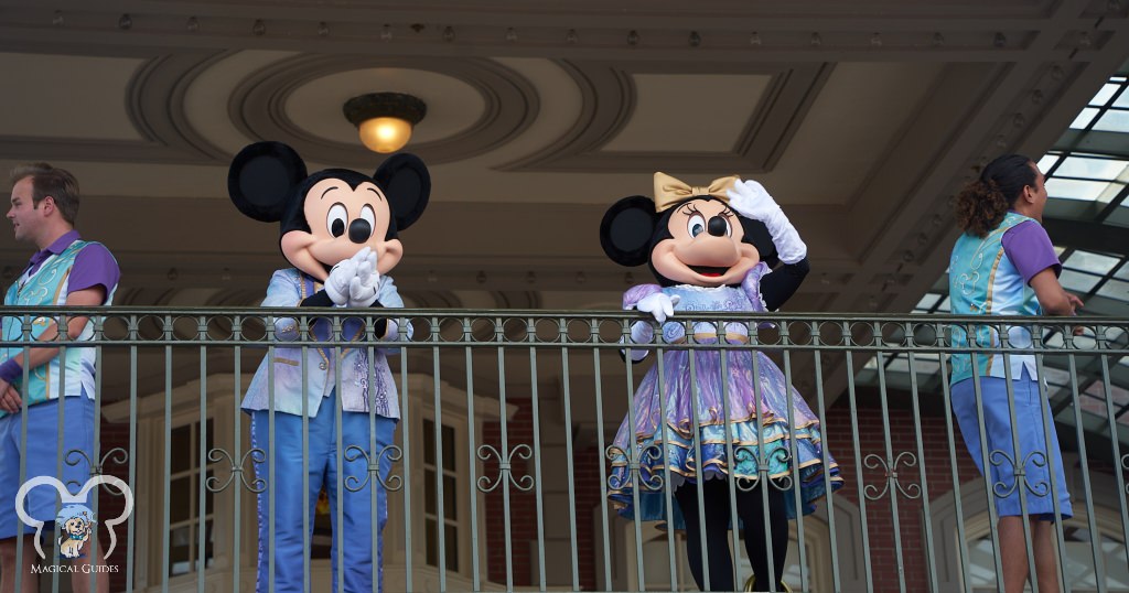 Mickey and Minnie waving to guests from the train station inside the Magic Kingdom.