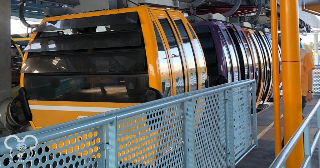 Disney's Skyliner gandola's coming into the station to pick up guests in bright colors with reflective coatings on the windows.