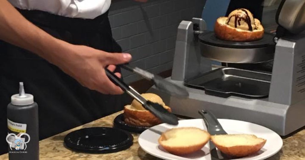 A cast member reaches for the top part of the brioche bun before pressing them together to make a one a Disney favorite treat.