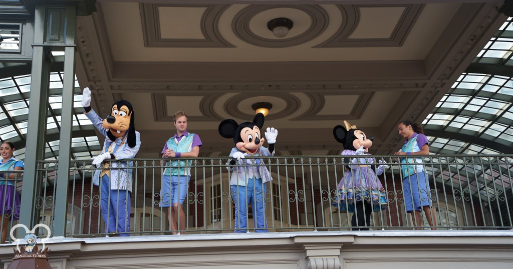 Goofy hanging out with Mickey and Minnie waving to the crowd below the train station in Magic Kingdom.