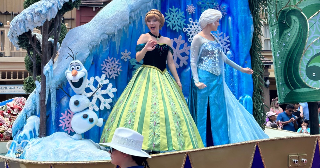 Queen Elsa and Princess Anna waving with Olaf as they pass during the Festival of Fantasy.